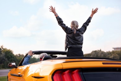 Photo of Senior couple enjoying cabriolet ride in city, back view. Woman with wide open arms