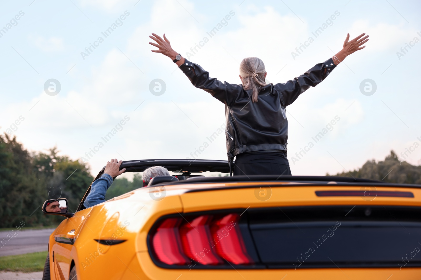 Photo of Senior couple enjoying cabriolet ride in city, back view. Woman with wide open arms