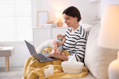 Photo of Telehealth. Smiling mother with her baby having online consultation with doctor by laptop on sofa at home