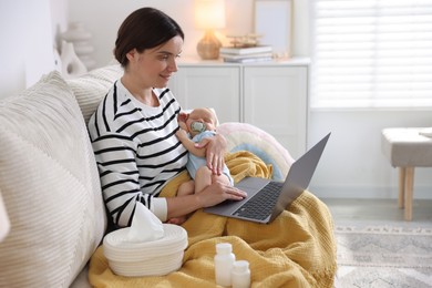 Photo of Telehealth. Smiling mother with her baby having online consultation with doctor by laptop on sofa at home
