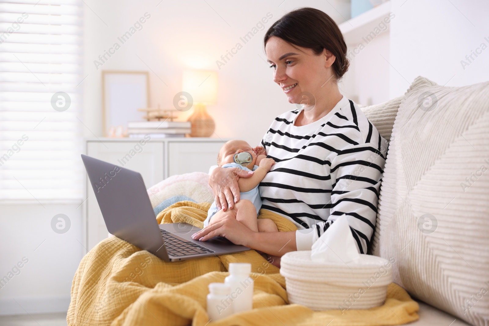 Photo of Telehealth. Smiling mother with her baby having online consultation with doctor by laptop on sofa at home