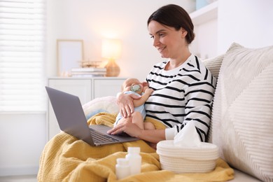 Photo of Telehealth. Smiling mother with her baby having online consultation with doctor by laptop on sofa at home