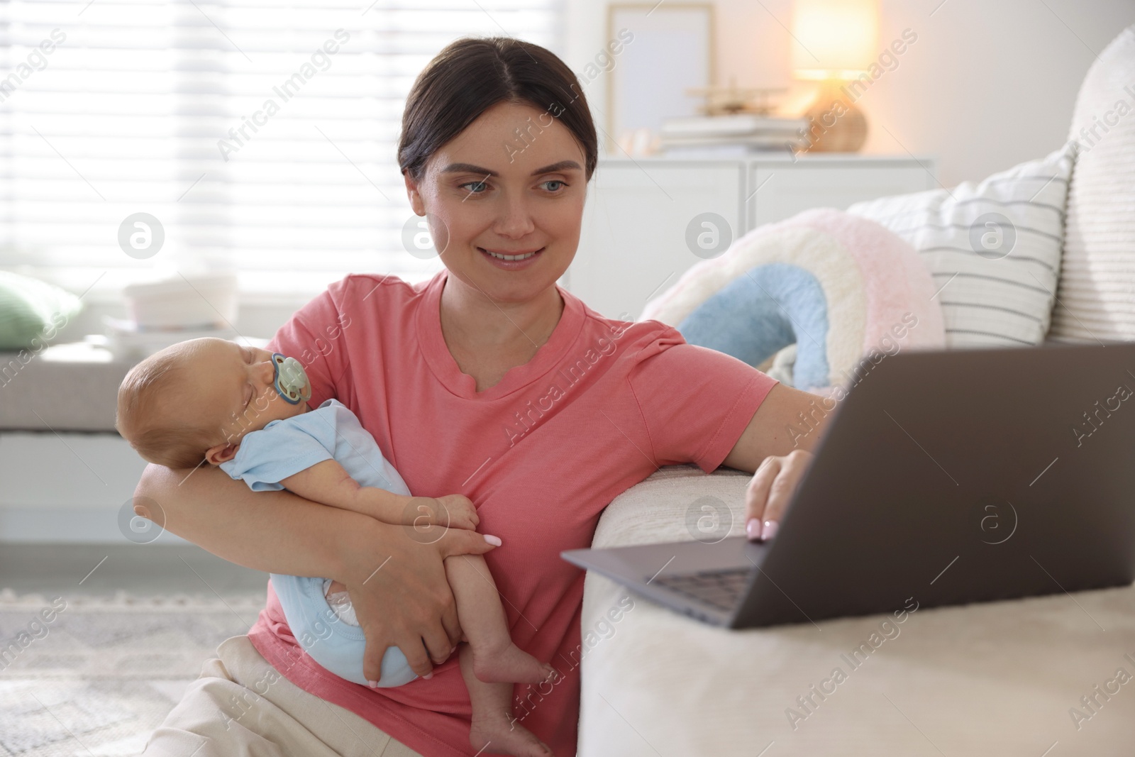 Photo of Telehealth. Smiling mother with her baby leaning on sofa and having online consultation with doctor at home
