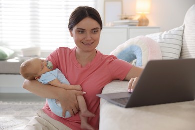 Photo of Telehealth. Smiling mother with her baby leaning on sofa and having online consultation with doctor at home