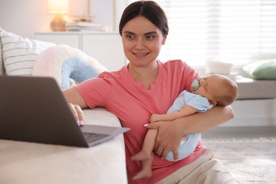 Photo of Telehealth. Smiling mother with her baby leaning on sofa and having online consultation with doctor at home
