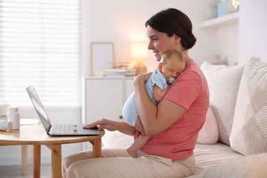 Photo of Telehealth. Smiling mother with her baby having online consultation with doctor by laptop on sofa at home