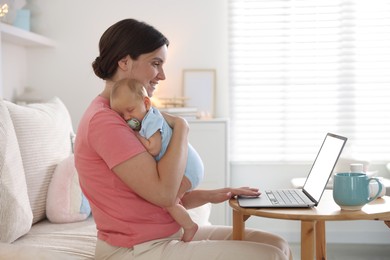 Photo of Telehealth. Smiling mother with her baby having online consultation with doctor by laptop on sofa at home