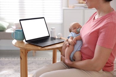 Photo of Telehealth. Mother with her baby having online consultation with doctor at table indoors, closeup