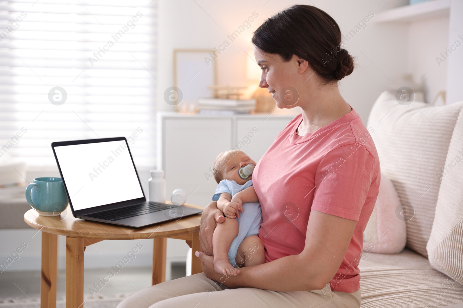 Photo of Telehealth. Smiling mother with her baby having online consultation with doctor by laptop on sofa at home