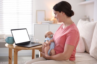Photo of Telehealth. Smiling mother with her baby having online consultation with doctor by laptop on sofa at home
