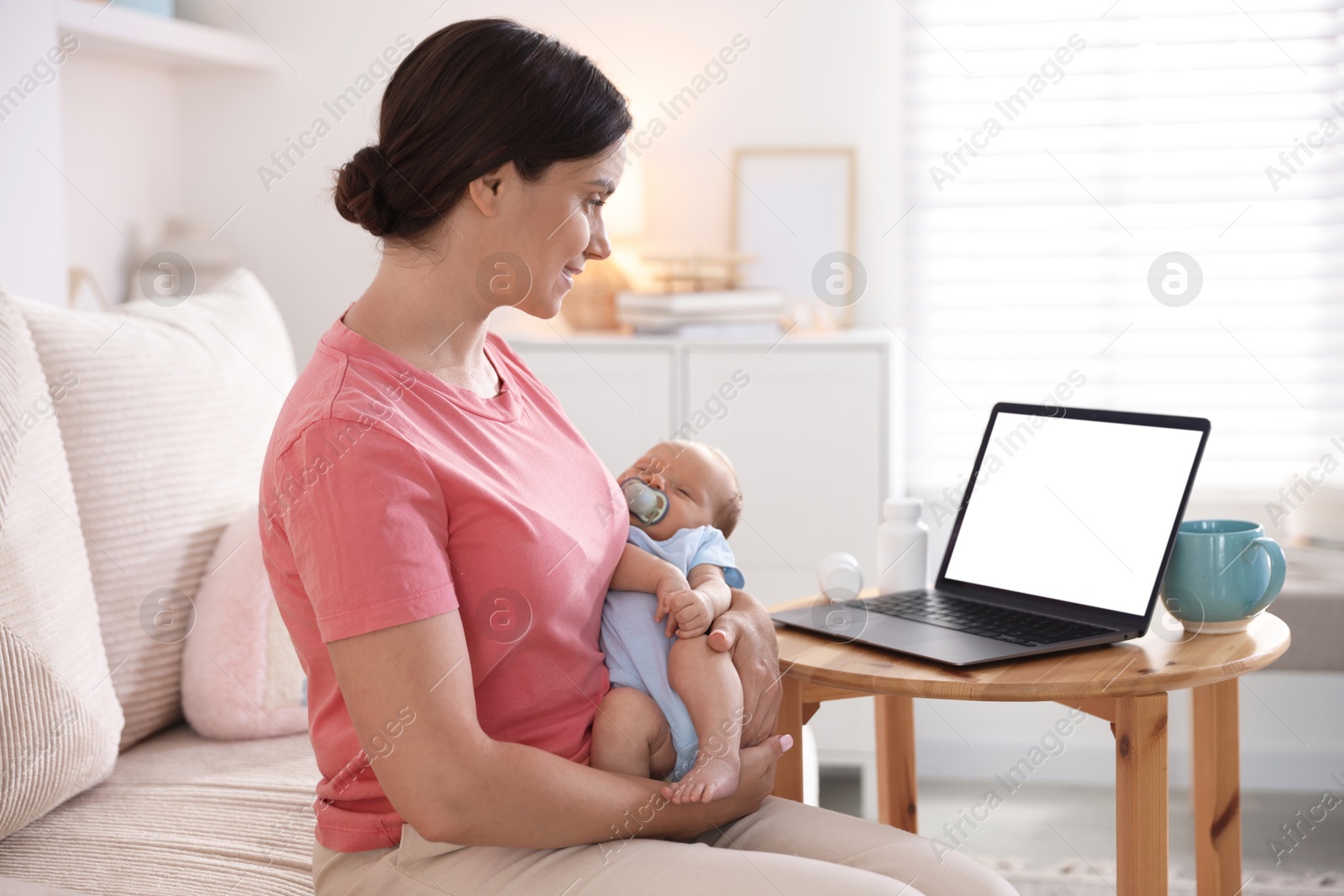 Photo of Telehealth. Smiling mother with her baby having online consultation with doctor by laptop on sofa at home