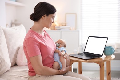 Photo of Telehealth. Smiling mother with her baby having online consultation with doctor by laptop on sofa at home