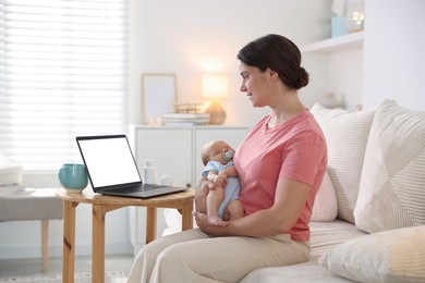 Photo of Telehealth. Smiling mother with her baby having online consultation with doctor by laptop on sofa at home