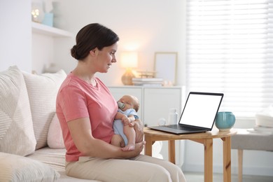 Photo of Telehealth. Smiling mother with her baby having online consultation with doctor by laptop on sofa at home