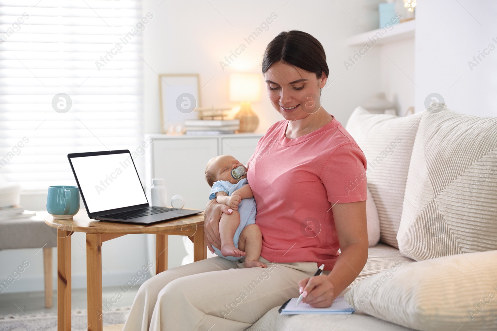 Photo of Telehealth. Smiling mother with her baby having online consultation with doctor by laptop on sofa at home
