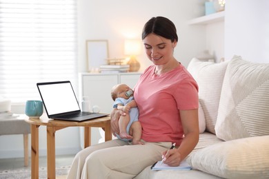 Photo of Telehealth. Smiling mother with her baby having online consultation with doctor by laptop on sofa at home