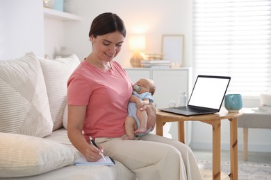 Photo of Telehealth. Smiling mother with her baby having online consultation with doctor by laptop on sofa at home