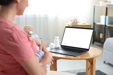 Photo of Telehealth. Mother with her baby having online consultation with doctor at table indoors, closeup