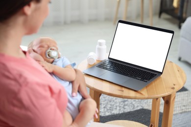 Photo of Telehealth. Mother with her baby having online consultation with doctor at table indoors, closeup