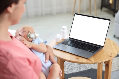 Photo of Telehealth. Mother with her baby having online consultation with doctor at table indoors, closeup