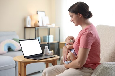 Photo of Telehealth. Smiling mother with her baby having online consultation with doctor by laptop on armchair at home