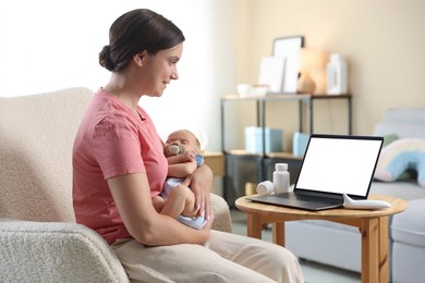 Photo of Telehealth. Smiling mother with her baby having online consultation with doctor by laptop on armchair at home