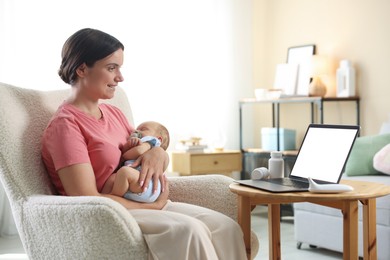 Photo of Telehealth. Smiling mother with her baby having online consultation with doctor by laptop on armchair at home
