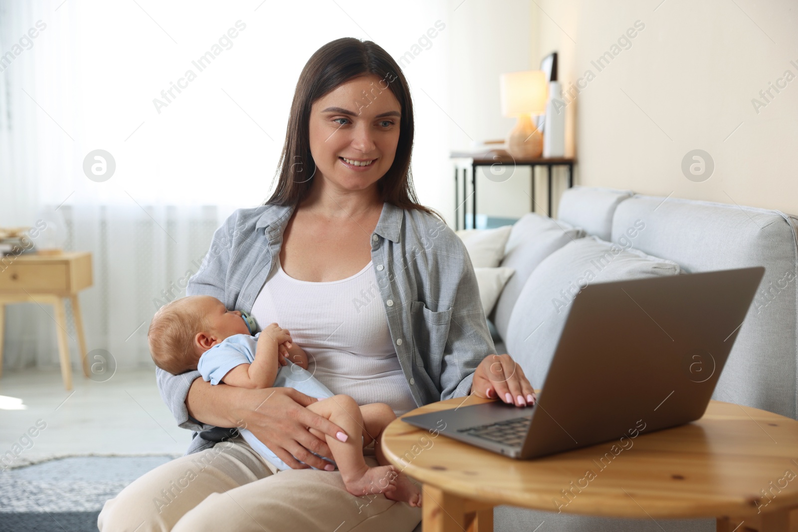 Photo of Telehealth. Smiling mother with her baby having online consultation with doctor at table indoors