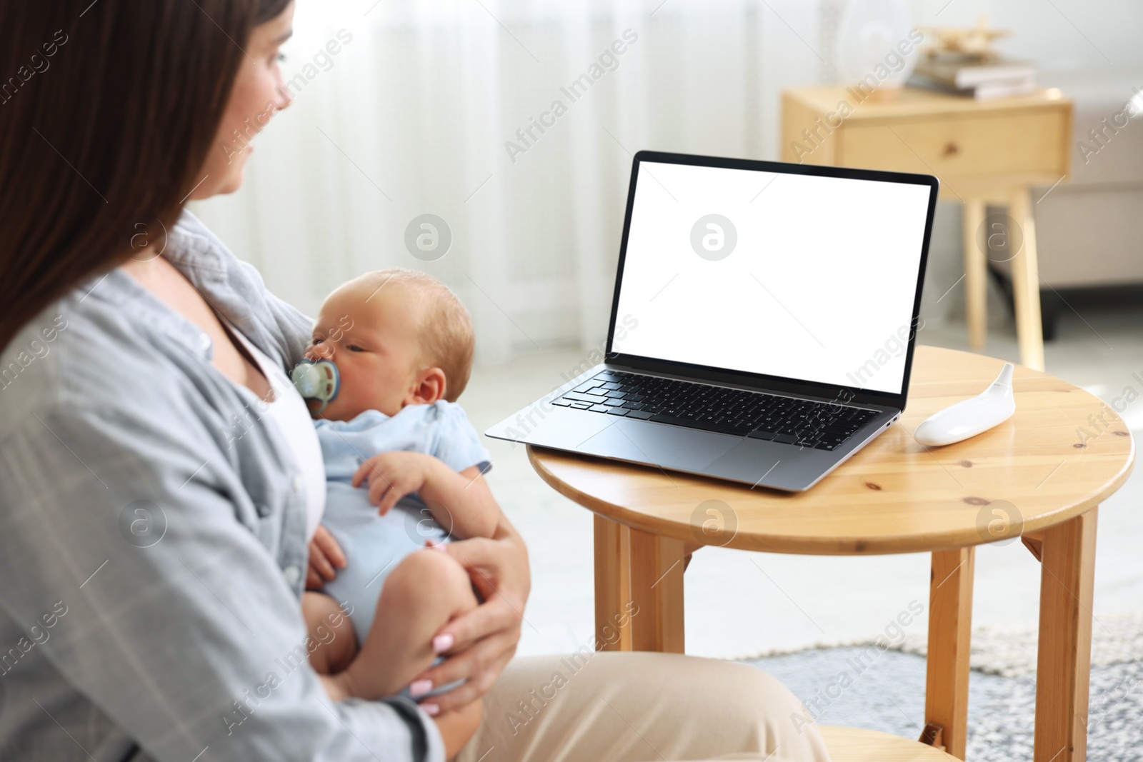 Photo of Telehealth. Mother with her baby having online consultation with doctor at table indoors, closeup
