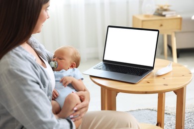 Photo of Telehealth. Mother with her baby having online consultation with doctor at table indoors, closeup