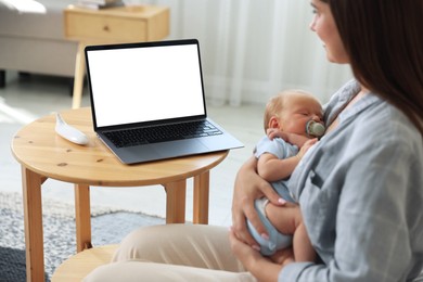 Photo of Telehealth. Mother with her baby having online consultation with doctor at table indoors, closeup