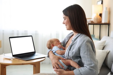 Photo of Telehealth. Smiling mother with her baby having online consultation with doctor on sofa indoors