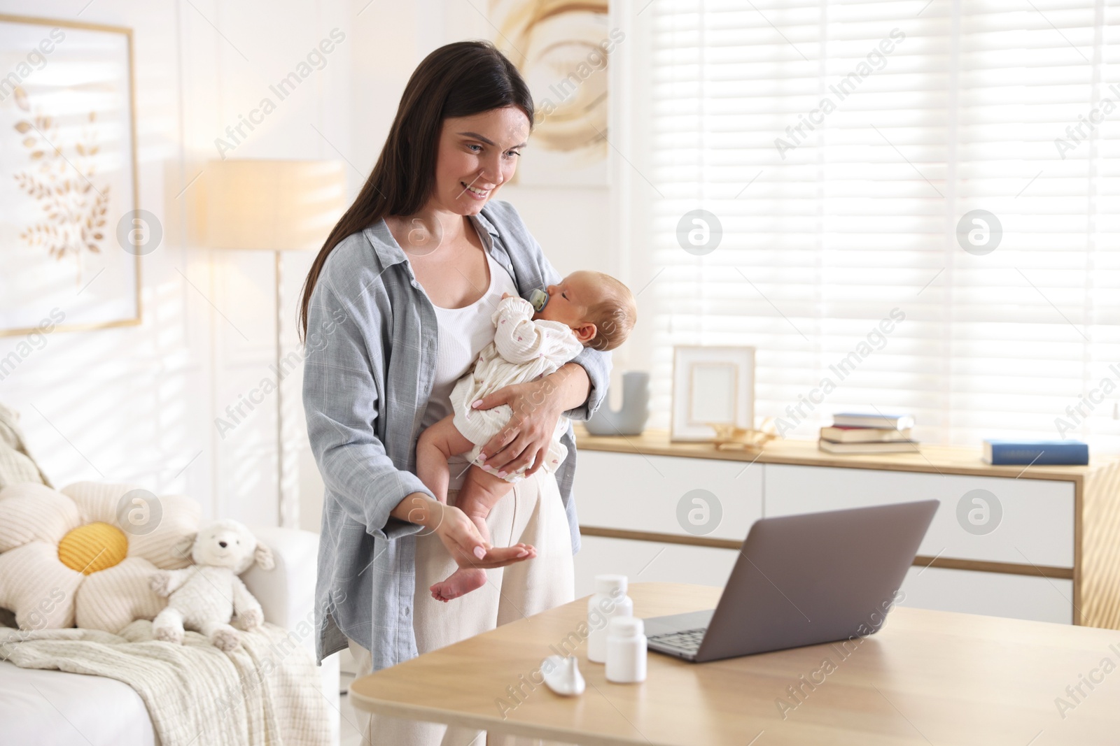 Photo of Telehealth. Smiling mother with her baby having online consultation with doctor at table indoors