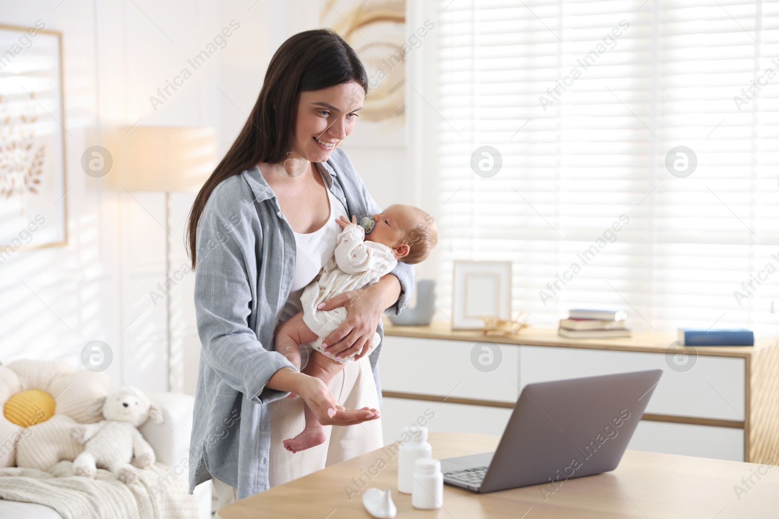 Photo of Telehealth. Smiling mother with her baby having online consultation with doctor at table indoors