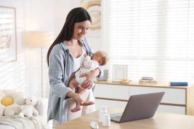 Photo of Telehealth. Smiling mother with her baby having online consultation with doctor at table indoors