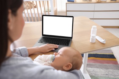 Photo of Telehealth. Mother with her baby having online consultation with doctor at table indoors, closeup