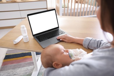 Photo of Telehealth. Mother with her baby having online consultation with doctor at table indoors, closeup