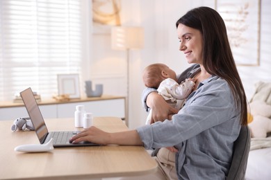 Photo of Telehealth. Smiling mother with her baby having online consultation with doctor at table indoors