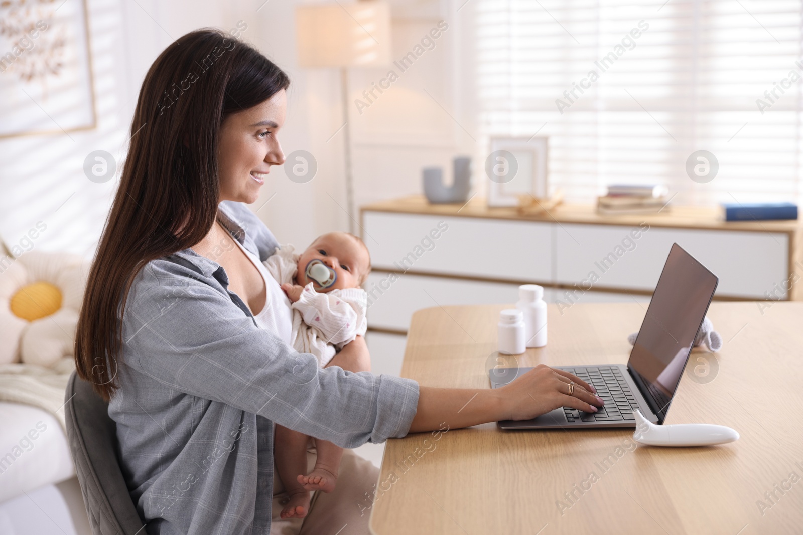 Photo of Telehealth. Smiling mother with her baby having online consultation with doctor at table indoors