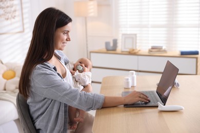 Photo of Telehealth. Smiling mother with her baby having online consultation with doctor at table indoors