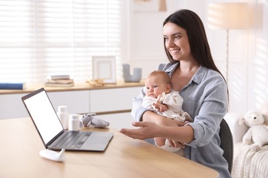Photo of Telehealth. Smiling mother with her baby having online consultation with doctor at table indoors
