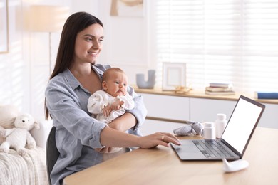Photo of Telehealth. Smiling mother with her baby having online consultation with doctor at table indoors
