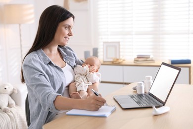 Photo of Telehealth. Smiling mother with her baby having online consultation with doctor and writing at table indoors