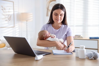 Photo of Telehealth. Smiling mother with her baby having online consultation with doctor and writing at table indoors