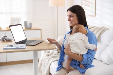 Photo of Telehealth. Smiling mother with her baby having online consultation with doctor by laptop on sofa at home