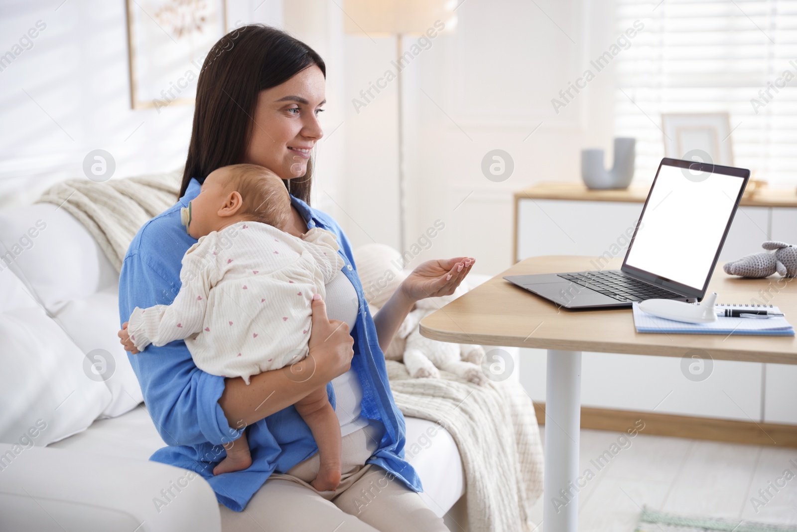 Photo of Telehealth. Smiling mother with her baby having online consultation with doctor by laptop on sofa at home