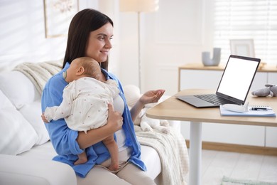 Photo of Telehealth. Smiling mother with her baby having online consultation with doctor by laptop on sofa at home
