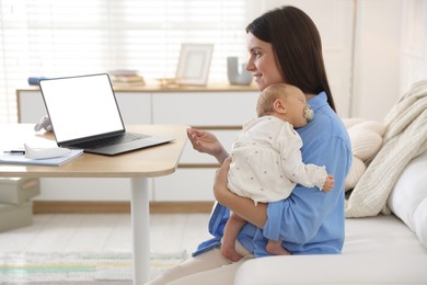 Photo of Telehealth. Smiling mother with her baby having online consultation with doctor by laptop on sofa at home