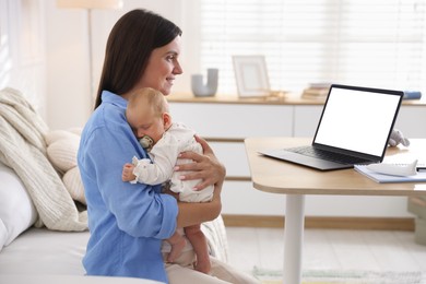 Photo of Telehealth. Smiling mother with her baby having online consultation with doctor by laptop on sofa at home
