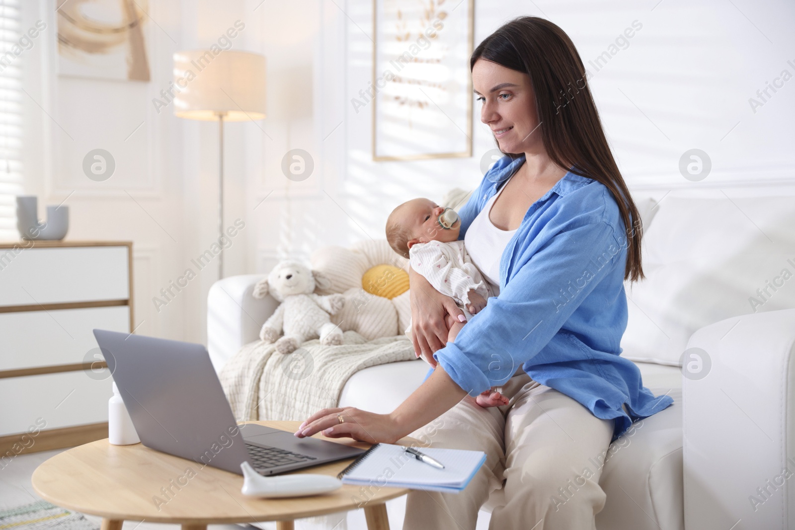 Photo of Telehealth. Smiling mother with her baby having online consultation with doctor by laptop on sofa at home